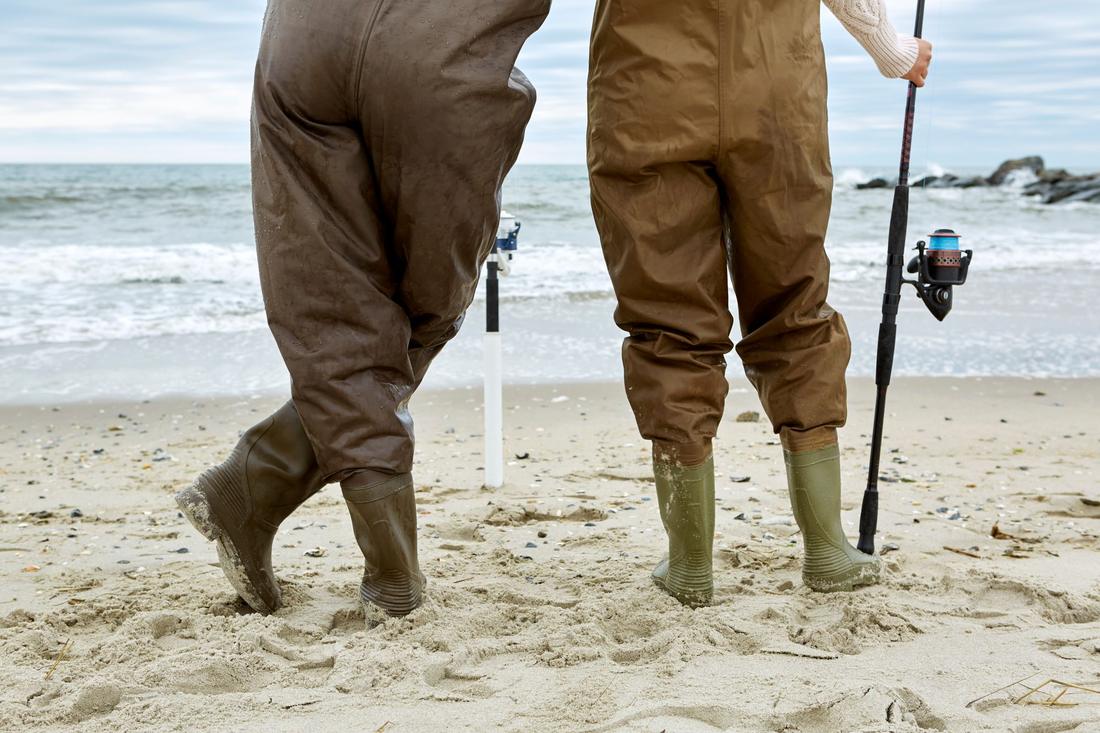Two anglers in waders standing on a beach with surf rods