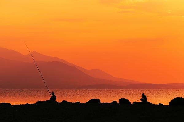 Two anglers casting from the rocks at sunrise