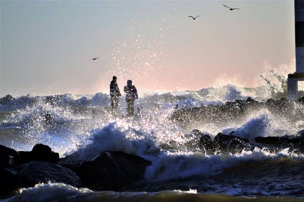 Two anglers on a jetty as waves crash around them