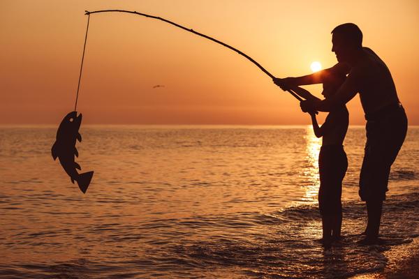 Silhouette of an adult and a child fishing together at sunset